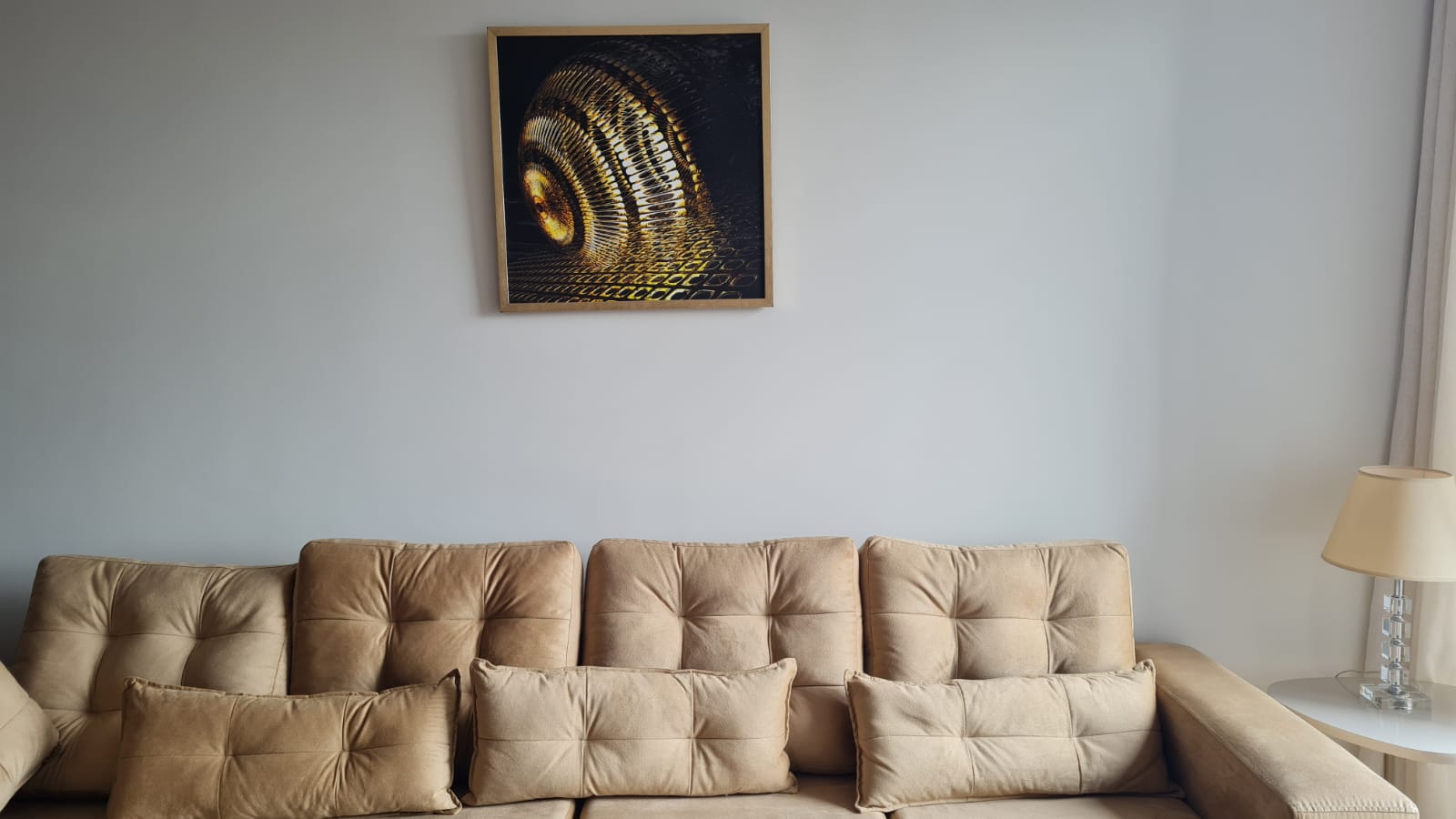 Obra dorada en espiral, Abstracción Volumétrica II de Vivianne Kieffer, en marco de madera sobre un sofá capitoné beige.