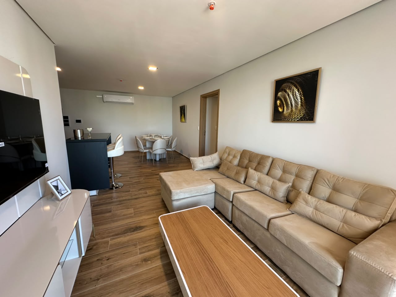 Sala con sofá esquinero beige, mesa de centro de madera y la obra en espiral sobre el muro.